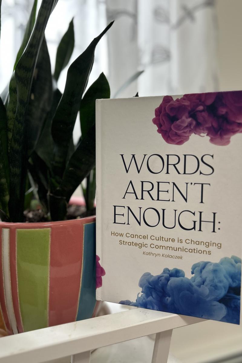 The book "Words Aren't Enough" is propped up beside a plant.